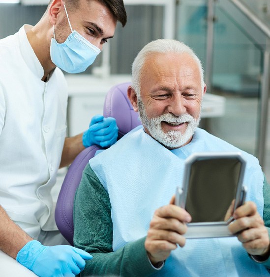 Man in dental chair smiling at reflection in mirror with masked dentist behind him