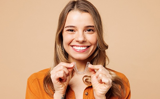 Woman in orange shirt holding clear aligner smiling