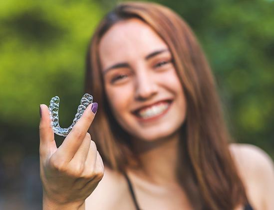 Woman with purple nails outside holding clear aligner