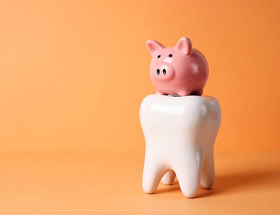Piggy bank sitting on large model tooth with orange background