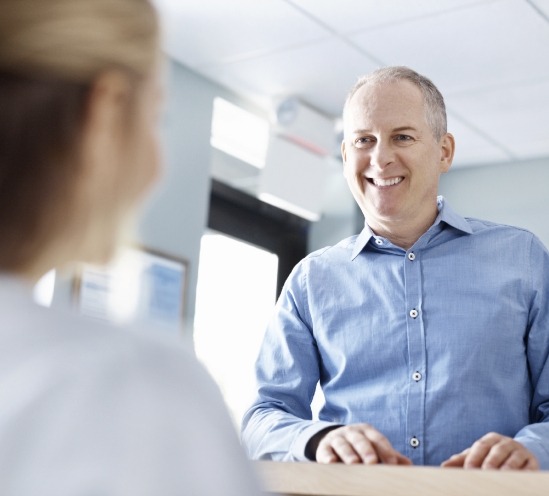 Man in blue collared shirt smiling at dental receptionist