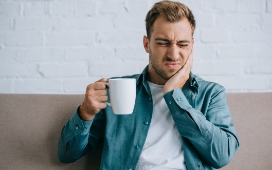 Man with coffee mug holding his cheek in pain