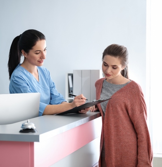 Dental receptionist showing a patient where to sign on clipboard