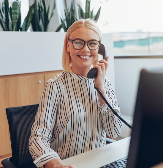 Smiling dental team member sitting at desk with computer and talking on phone