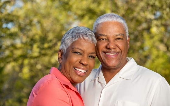 Senior man and woman smiling outdoors after replacing missing teeth in Fresno