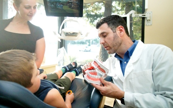 Dentist showing young boy in dental chair a model of the mouth