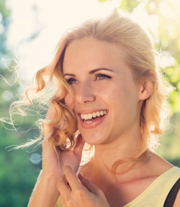 Woman with curly blonde hair grinning on sunny day
