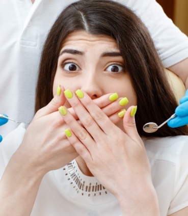 Woman in dental chair fearfully covering her mouth with her hands