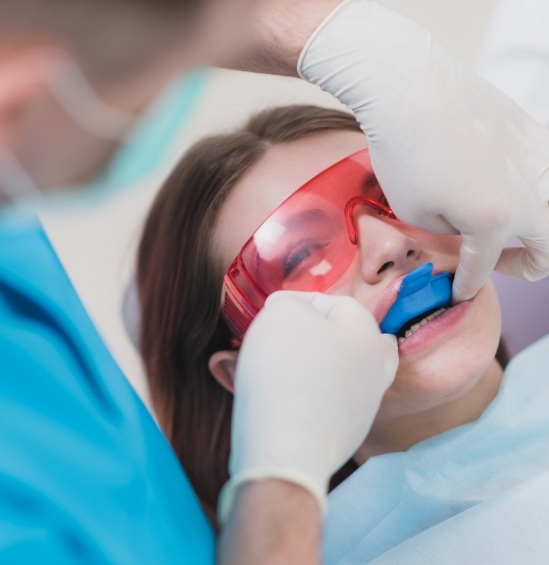 Young woman having fluoride tray placed over her teeth in dental chair