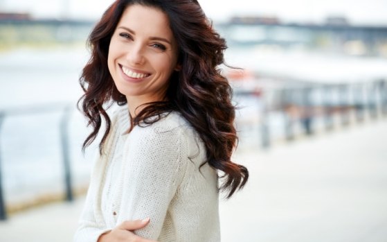 Woman in white sweater grinning outdoors after sedation dentistry in Fresno