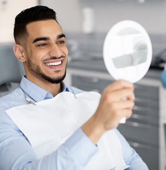 Man smiling at reflection in handheld mirror